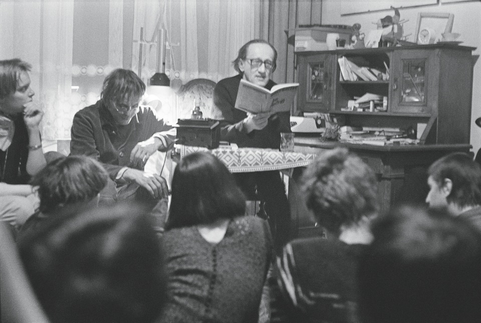 Magdeburg, DDR, 1983. Theaterregisseur Heiner Müller (met boek) en Sascha Anderson (links van hem) bij een literaire huiskamerbijeenkomst. Foto: Harald Hauswald / Ostkreuz